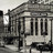Static grayscale image of a building facade with columns and a curved roofline, showing architectural details and a streetlamp.