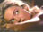 Pixelated close-up of a person's face with light skin tone, brown hair, and closed eyes against dark background.
