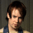 Pixelated close-up of a person with brown hair and light skin, wearing a dark blue garment against a muted background.