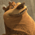Pixelated brown cartoon animal with large eyes and a wide open mouth, standing against a muted gray background.