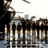 Static pixelated image of a figure in dark clothing holding an object near a cityscape with water reflections, rendered at low resolution.