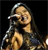 A pixelated figure with long dark hair holds a microphone near their mouth against a black background.