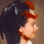 Pixelated profile view of a person with dark hair and red highlights, wearing a red headband, against a brown background.