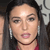 A pixelated close-up of a person with dark hair, silver hoop earrings, and a red garment visible at the bottom edge.
