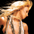 Pixelated image of a person with long blonde hair flowing left to right, wearing a white sleeveless top against a black background.