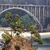 Static pixelated image showing a bridge structure with green foliage and brown ground elements under a blue sky background.