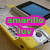 A yellow and silver handheld device with a blue screen displays text in different colors across four