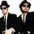 Two pixelated figures in black suits and sunglasses stand against a split background of white and cyan, with bold text reading "I love the 80's" on the right.