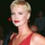 Pixelated close-up of a person with short blonde hair wearing a red sleeveless top against a dark background.