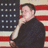 A pixelated figure in a black shirt stands before an American flag, hand raised to face in a gesture.
