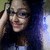 Pixelated image of a person with long dark hair, wearing glasses and a black top, holding an object near their head against a gradient background.