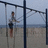 Pixelated static image shows a person on a beach with playground equipment, wearing dark shorts and light shirt against sandy background.