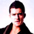 Static pixelated image of a person with short dark hair wearing a black jacket over an open shirt against a light background.