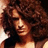 Pixelated close-up of a person with voluminous curly hair, wearing dark clothing against warm-toned background.