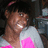 Pixelated image of a person with dark hair wearing a white and pink top, smiling broadly against a dark background.