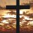 A dark cross stands against a pixelated background of warm brown and orange tones with scattered light patches.