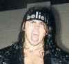 A person with long dark hair wears a black headband with white text, a black leather jacket, and a light-colored shirt, with a dark star-shaped overlay containing text.