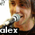 A person with brown hair sings into a silver microphone, with text overlays reading 'alex' and 'gaskarth' in white letters on black bars.