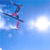 Pixelated static icon of a skier in mid-air against a blue sky background with white cloud-like shapes.