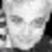 A grayscale pixelated image of a human face with neutral expression, featuring visible eyes and nose against a light background.