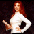 A pixelated image of a woman with long red hair wearing a white top, holding an object in her right hand and resting the other on her hip against a dark background.