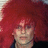 Pixelated static image of a person with voluminous red hair and light skin, wearing dark clothing against a solid background.