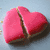 A heart-shaped object with pink icing and a brown base, split into two pieces on a light blue background, with text appearing sequentially across frames.