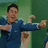 A person in a blue suit with arms extended, making a thumbs-up gesture and pointing forward against a green background.
