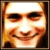 Pixelated static image of a person's face with warm color tones and visible dithering, framed by dark borders on the left and right sides.