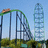 Pixelated image of a green roller coaster with a loop and lift hill at an amusement park, under blue sky.