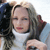 A pixelated close-up of a person with light brown hair wearing a white top, partially obscured by another figure in dark clothing.