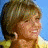 A pixelated image of a person with short brown hair smiling, wearing a yellow garment against blue and gold backgrounds.