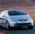 A light blue sedan with dark blue windows and black wheels is positioned on a reflective surface under a gradient sky.