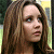 Pixelated close-up of a person with long brown hair, light skin, and visible facial features against a blurred background.