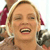 A pixelated close-up of a person with light brown hair wearing a red headband, smiling with eyes closed and mouth open showing teeth, holding a dark object near the face.