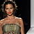 Pixelated static image of a person with dark hair wearing a strapless dress and choker necklace against a dark background.