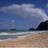 Pixelated beach scene with blue sky, white clouds, greenish water, and brown sand under a dark landmass on the right.