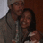 A static image of two people embracing, one wearing a gray hoodie and beanie, the other with long dark hair in a light-colored top.