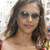 A pixelated close-up of a person with long dark hair wearing dark sunglasses and a light-colored top against a blurred background.