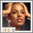Pixelated portrait of a person with light brown hair styled up, wearing earrings, against a dark background with 'alicia' text below.