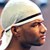 Pixelated static image of a person wearing a white cap with black stripe in profile view, showing partial face and neck against blurred background.