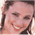 Pixelated close-up of a person's face with light skin tone, dark hair, and a broad smile showing teeth, set against a light background.