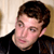 Static pixelated image of a person with short brown hair wearing a black top against a light background.