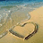 A pixelated beach scene with a heart shape drawn in the sand, waves lapping at the shore, and a gradient sky transitioning from blue to beige.