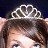 A pixelated close-up of a person wearing a silver tiara with heart-shaped cutouts against a dark background.