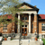 Pixelated image of a classical building with columns, red roof, and greenery under a blue sky.