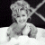 Pixelated grayscale image of a person with light-colored hair styled in an updo, wearing a white garment against dark and light backgrounds.
