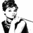 Pixelated grayscale icon of a person with short dark hair, wearing a suit and tie, holding an object near their mouth.