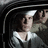 Pixelated static image of a person with dark hair wearing a white-collared shirt, positioned inside what appears to be a vehicle interior.