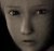 Pixelated close-up of a human face with neutral expression, dark background, and visible eyes nose mouth.